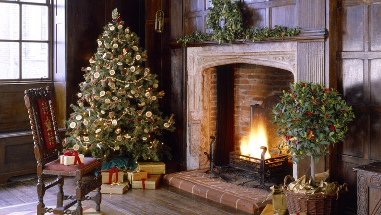 A Christmas tree and presents next to a glowing fire, in a wooden panelled room, at Sutton House in Hackney.